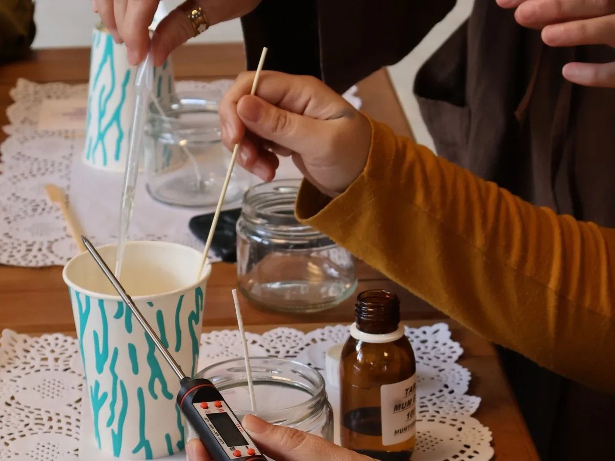 Manos trabajando la cera y midiendo la temperatura en un taller de velas